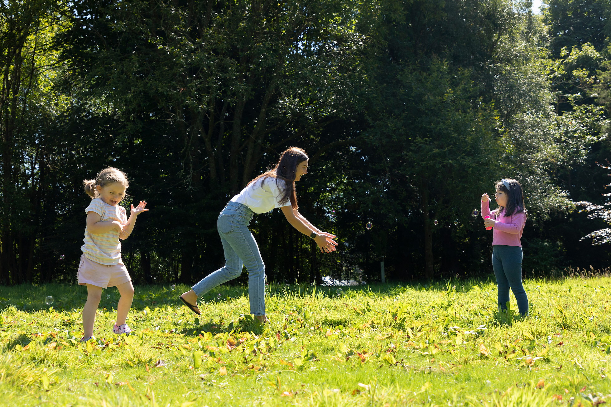 Mother and two young girls playing with bubbles in woodland glade, Dunblane