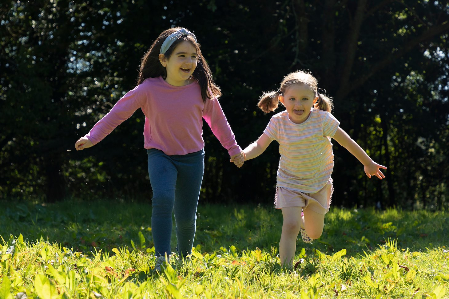 Two young girls running across woodlland glade, Dunblane