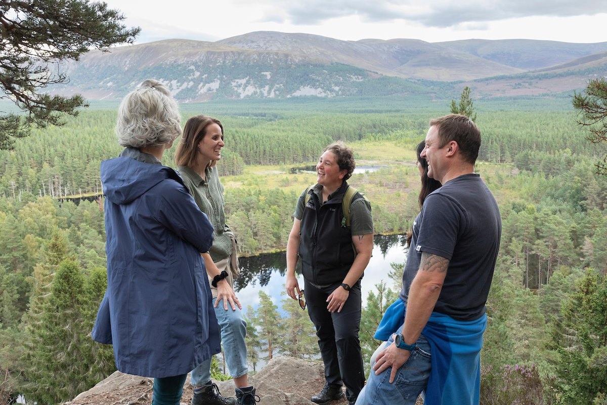 Rewilding Journeys guide, Stef Lauer, talking to guests at a viewpoint in the forest overlooking Uath Lochans in the Cairngorms National Park