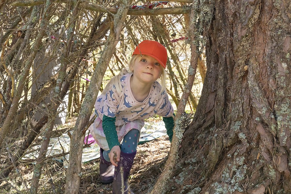 Young girl in natural 'den' in woodland as part of 'RESTORE' - a community woodland crafts and skills project at Lynamer, a Northwoods Rewilding Network land partner, Nethybridge, Cairngorms National Park, April 2023